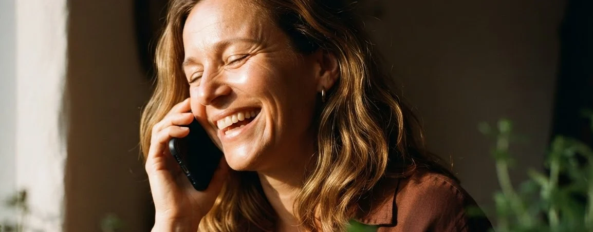 Une femme qui rit au téléphone près d'une fenêtre baignée de soleil